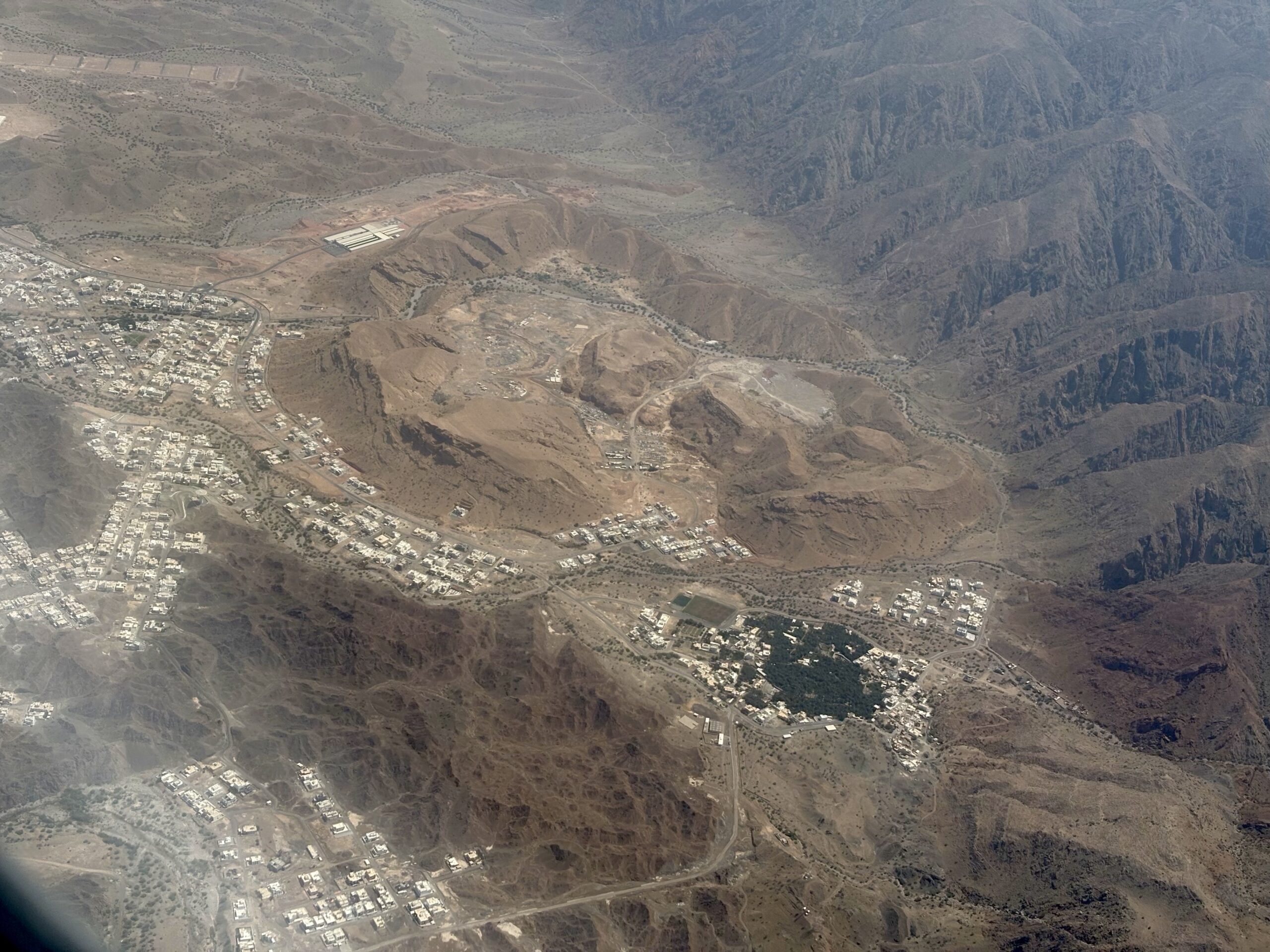 Aerial view of a dry, hilly landscape with a small town clustered along the bottom left and winding roads crossing the terrain.