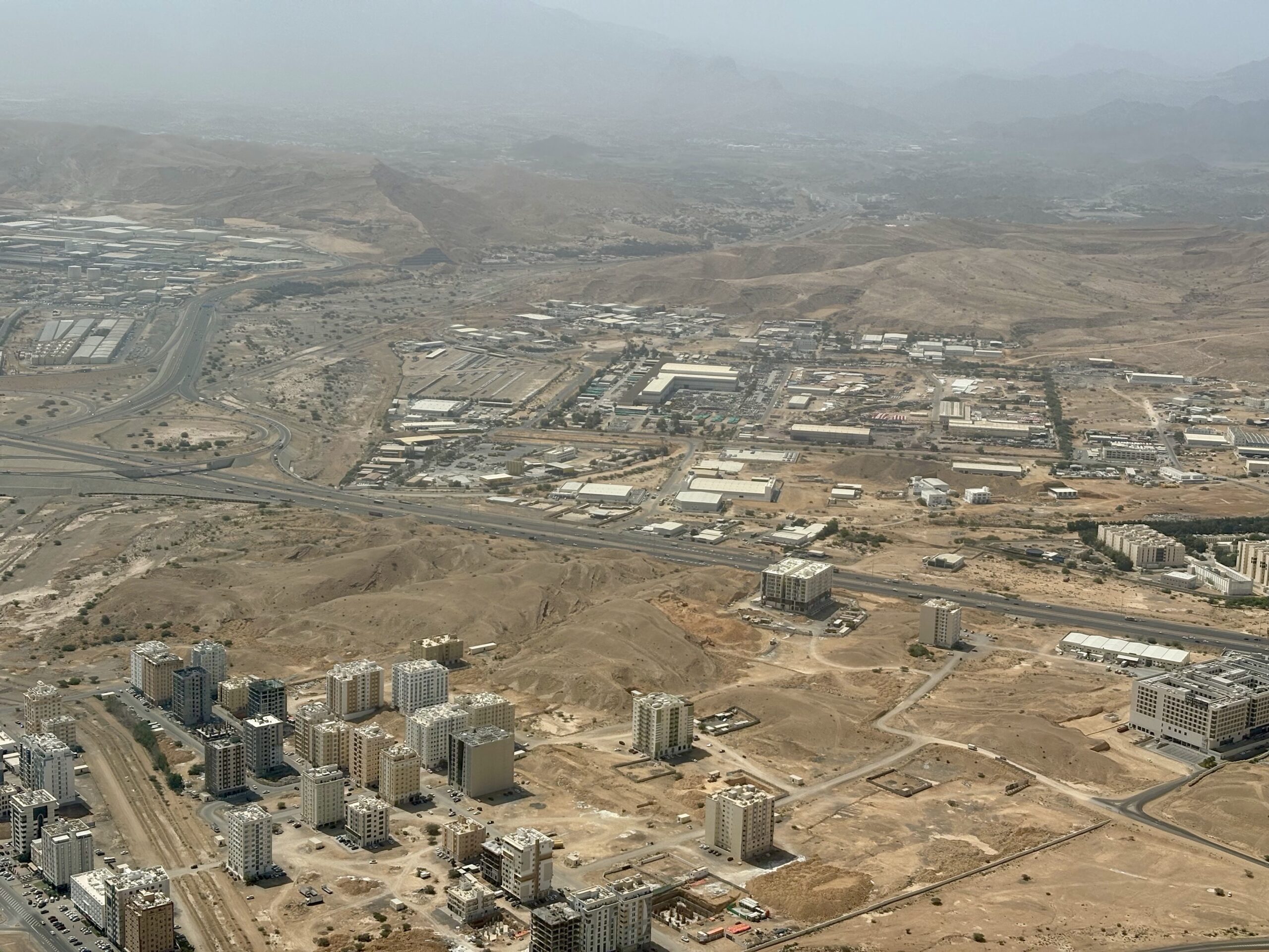 A sprawling desert city with numerous mid-rise apartment blocks under construction and a network of highways in a barren landscape.