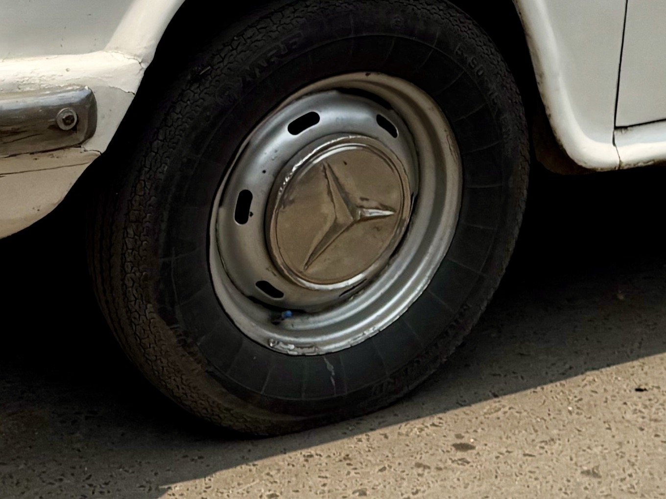 Close-up of a vintage car wheel with a metal hubcap and black tire on pavement.