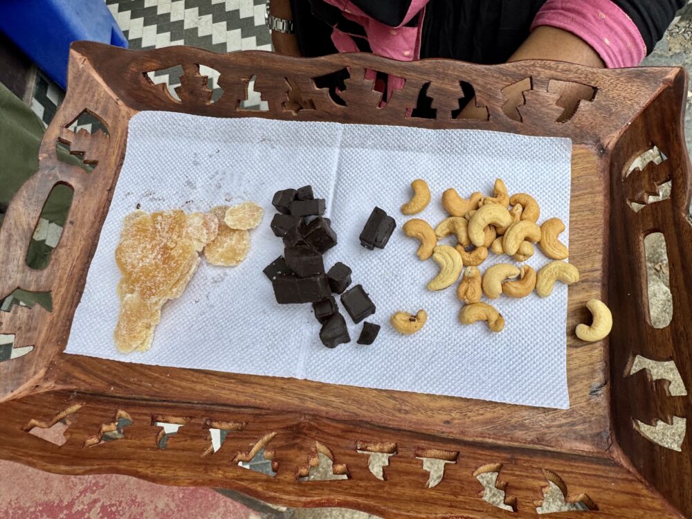 Candied fruit, dark chocolate chunks, and cashews arranged on a white napkin in a carved wooden tray.