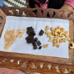 Candied fruit, dark chocolate chunks, and cashews arranged on a white napkin in a carved wooden tray.