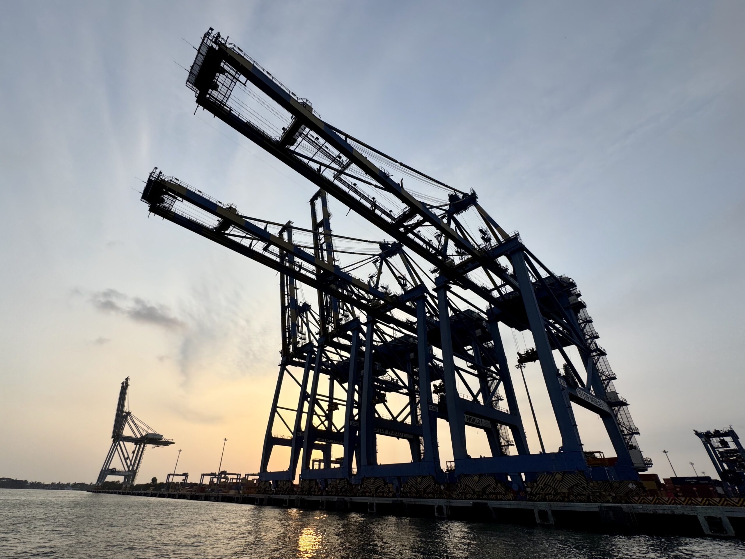 Silhouetted construction crane framework over a harbor at sunset venturing into the sky