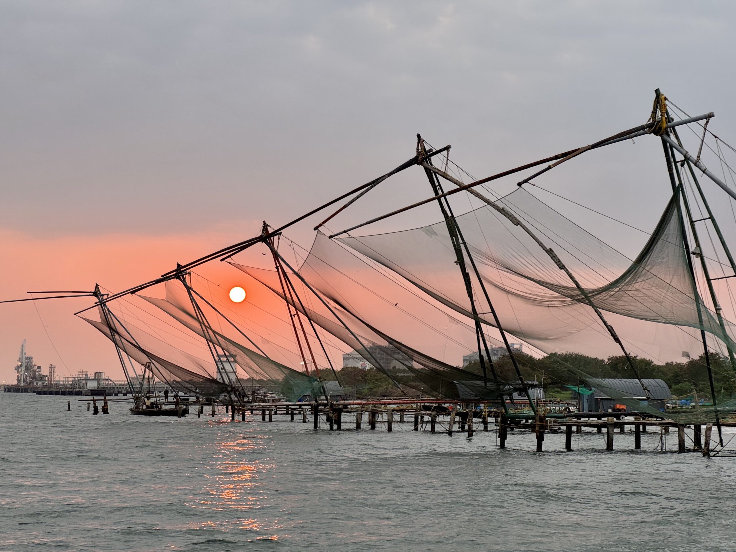 Sunset over a harbor with large fishing nets stretched between poles, metal frames, and a calm water foreground.