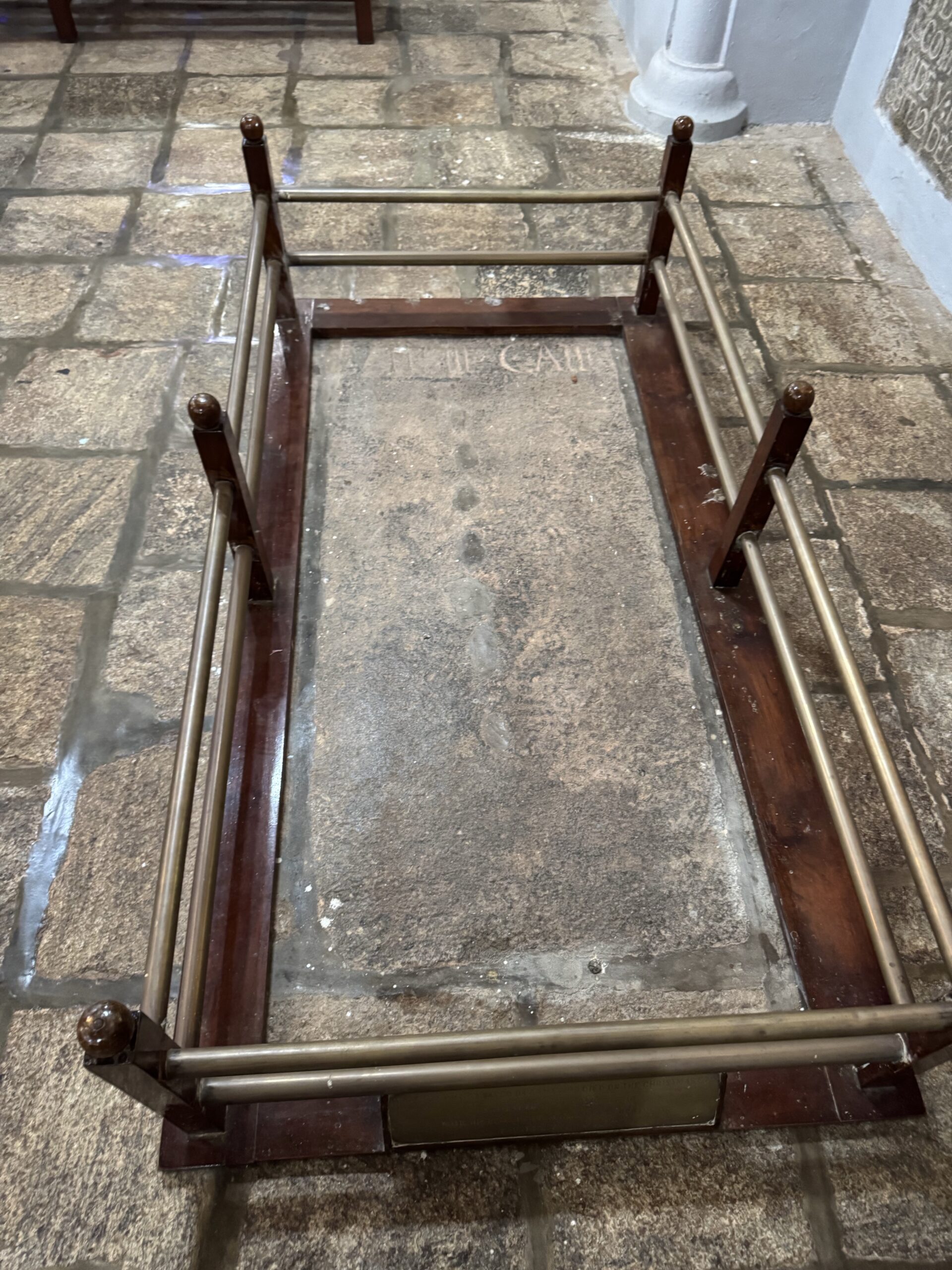 Square metal railing surrounding an empty rectangular opening in a stone floor, resembling a small trap or pit in a historic interior.