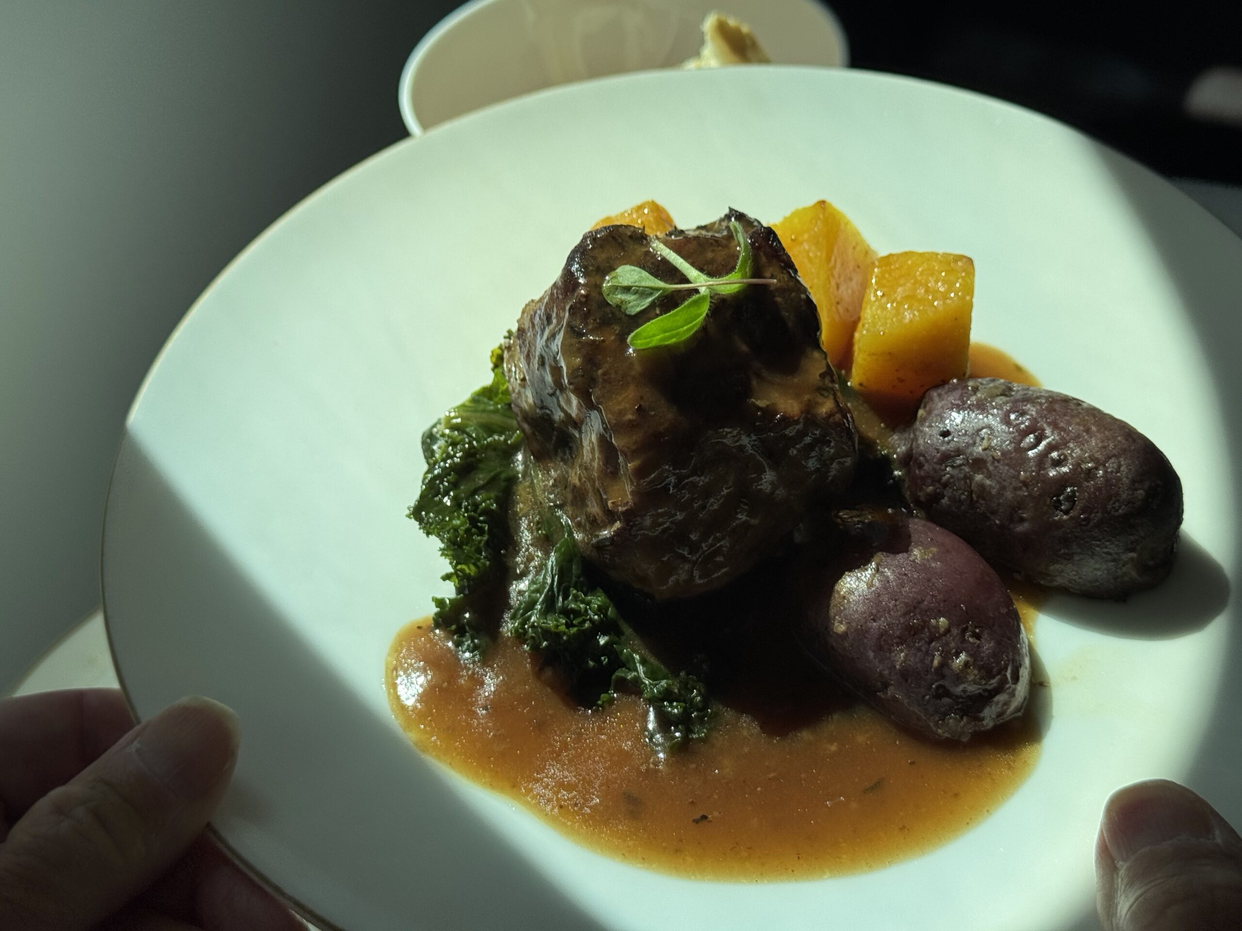 Plate of roasted meat with greens, purple potatoes, and orange sauce, garnished with a herb sprig.